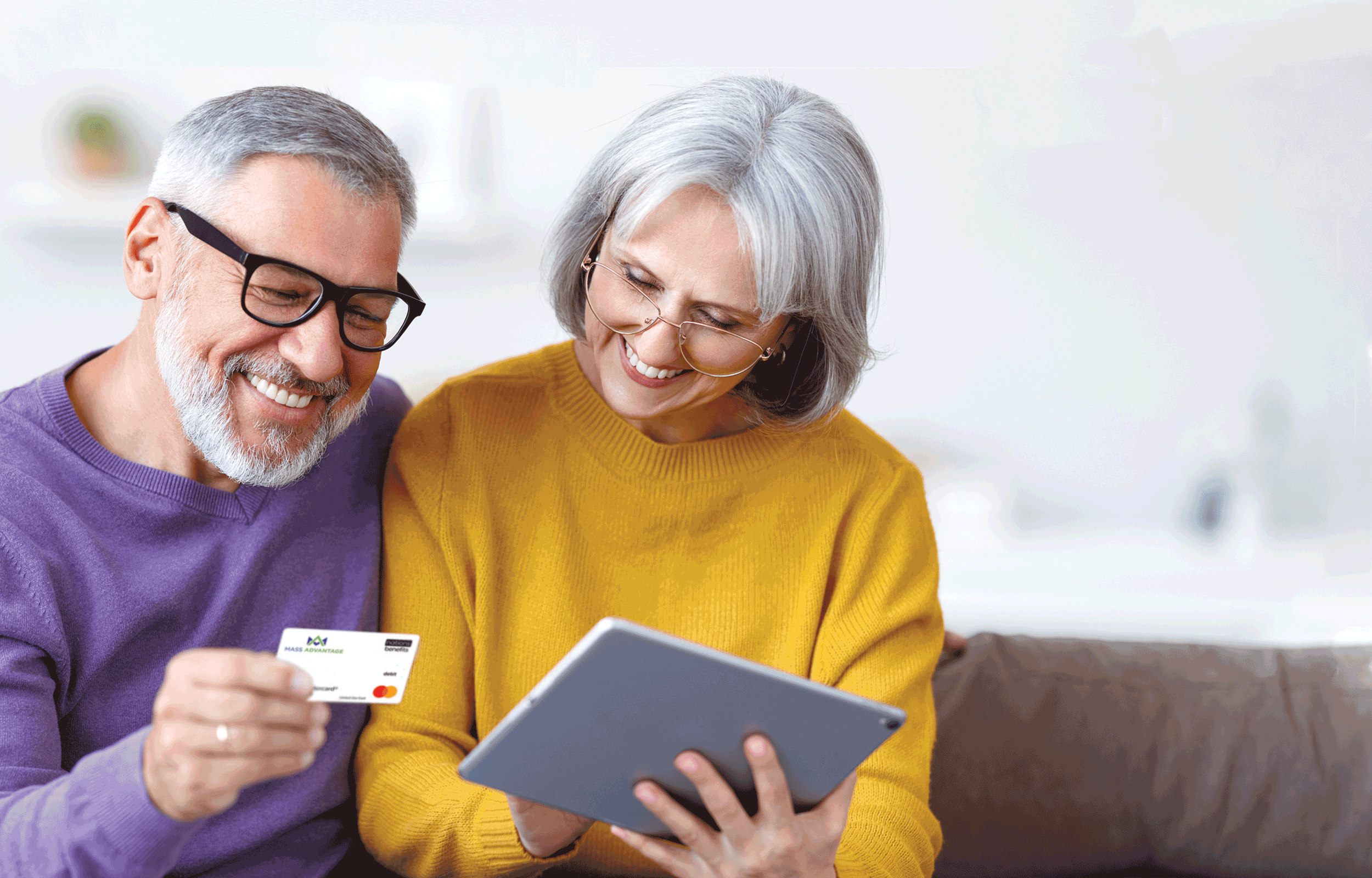 A man in a purple shirt and a woman in a yellow shirt are looking at a tablet and benefit card.