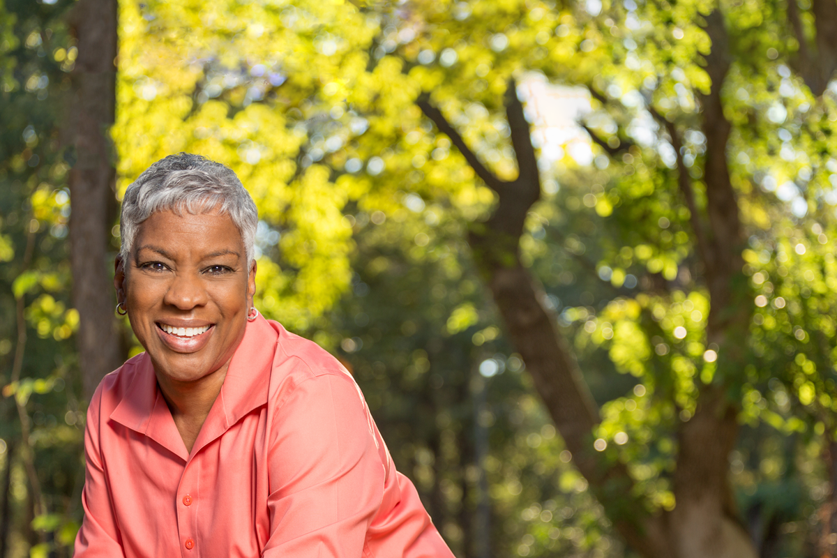 A woman in a pink shirt is shown in front of trees.