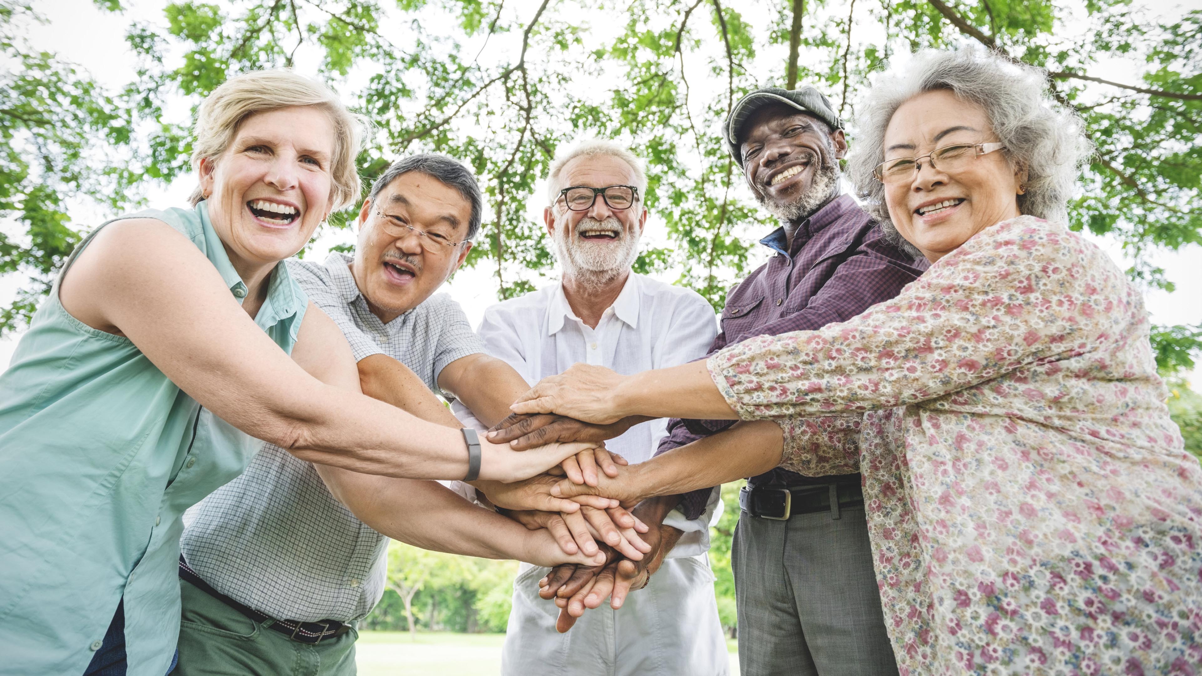 A group of happy seniors have their hands in the middle of a semi-circle.