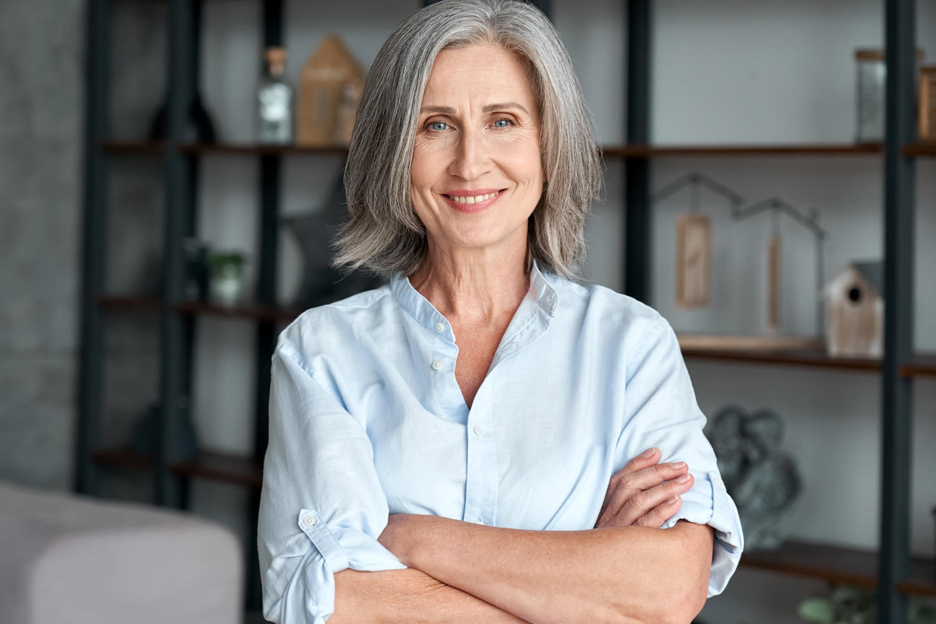 A woman in a blue shirt is standing in front of a shelf with decorations.